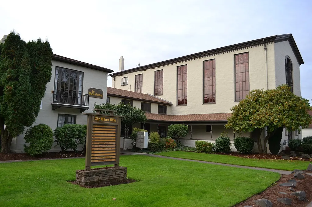 The First Congregational Church building in Eugene, Oregon. The building was later renamed the Willcox building, after architect Walter R. B. Willcox. Note: The two signs visible in this photo use the spelling "Wilcox", and that is a change to the same two signs as visible in 1979 photos linked from the Wikipedia article, as part of the NRHP nomination, but the change appears to have been made in error. The April 21, 1947 Oregonian newspaper obituary for Mr. Willcox uses a two-L spelling, and a memorial sculpture of Mr. Willcox at the University of Oregon (where he was a longtime professor) is identified with the spelling "Willcox".