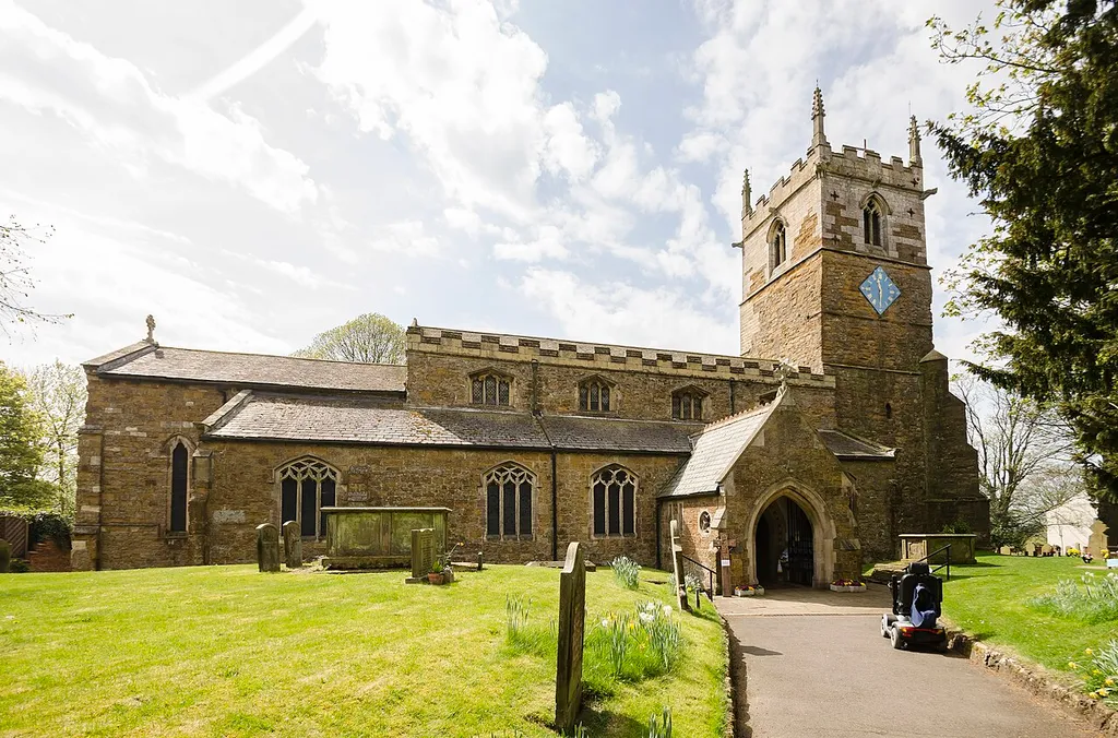 The church dates from the 11th century onwards and was rebuilt and restored in the 19th century. Certainly there was a church here in Saxon times and the lower part of the tower is probably Saxon, from around 1050. There is a west tower, nave with clerestory and north and south aisles, north porch, vestry and chancel. The tower is built in ironstone and dates from the mid-12th century. It is thought that the lower stage the tower could have been a Norman porch to the old church. The second stage is Early English and the top stage is Perpendicular. The tower has an embattled parapet with pinnacles and gargoyles. The tower arch has zigzag decoration. There are eight bells. The nave has four-bay arcades with octagonal piers and four clerestory windows either side. The chancel arch is from the 13th century. It is thought that the church may have been intended as being a cruciform shape with a crossing, or it may indeed have once been like this. The chancel was largely rebuilt in 1848 and restored in 1873. The reredos is from that date. There are several effigies of Knights set into arched tombs in the wall. There is a triple lancet east window, and stained glass from a variety of makers. The organ is by Cousans, and was installed in 1885. The rood beam is by Wilfrid Bond, erected in 1929. This is a photo of listed building number 1063382.
