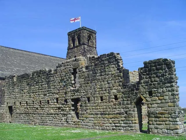Surviving wall of the west range of St Paul's Monastery, Jarrow, Tyne and Wear, seen from the southwest. In the background is the Norman tower of St Paul's parish church