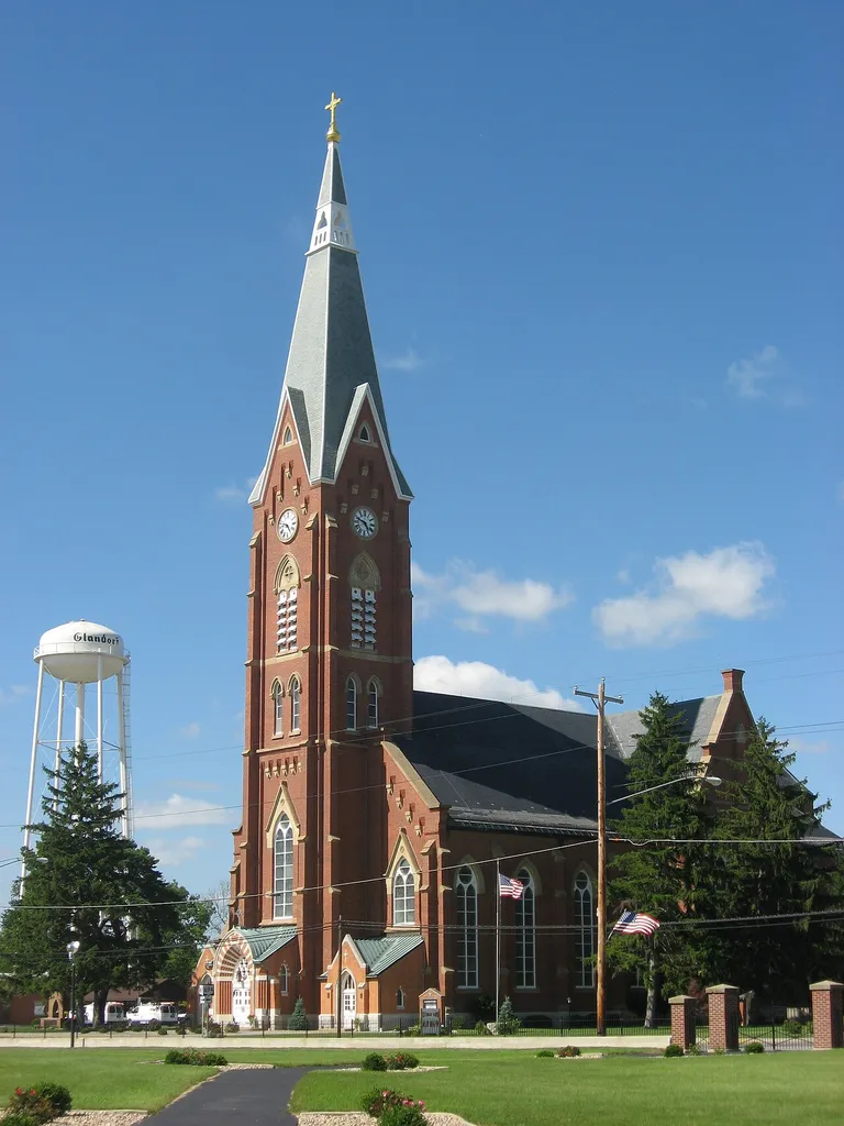 Front and southern side of St. John the Baptist Catholic Church, located at the intersection of Main (State Route 694) and Horstmann Streets in Glandorf, Ohio, United States. Built in 1875, it is listed on the National Register of Historic Places. Photo is taken from a pathway in the old parish cemetery, across Main Street from the church.