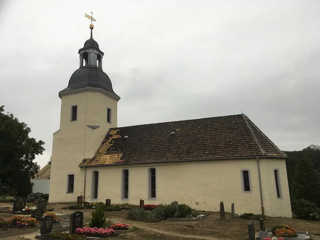 Village church with interior and churchyard cemetry in Dahlenberg (Trossin), Main street (german: Hauptstraße), single-aisled hall church: plastered quarry stone construction, gable roof, crown tail cover, basket arch window with flaps, square west tower, oktogonal-shaped in the bell floor, above hood (slate cover), lantern (zinc sheet) inscribed 1781 with segmental arch openings, ball attachment, weather vane and cross, 3/8 choir closure, inside 3-sided wooden gallery, organ gallery with openwork parapet, pulpit renewed in the 20th century (balustrades: depictions of the evangelists around 1620), commemorative plaque inscribed in 1620 (Predella depicting the sacrament and crucifixion, kneeling donor family), wooden crucifix (unmounted/early 20th century).
