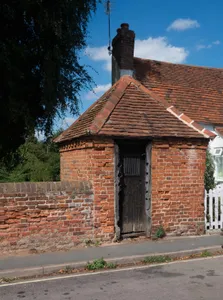 Village lock up with stocks and whipping post attached to doorframe, south east corner of churchyard of St Thomas