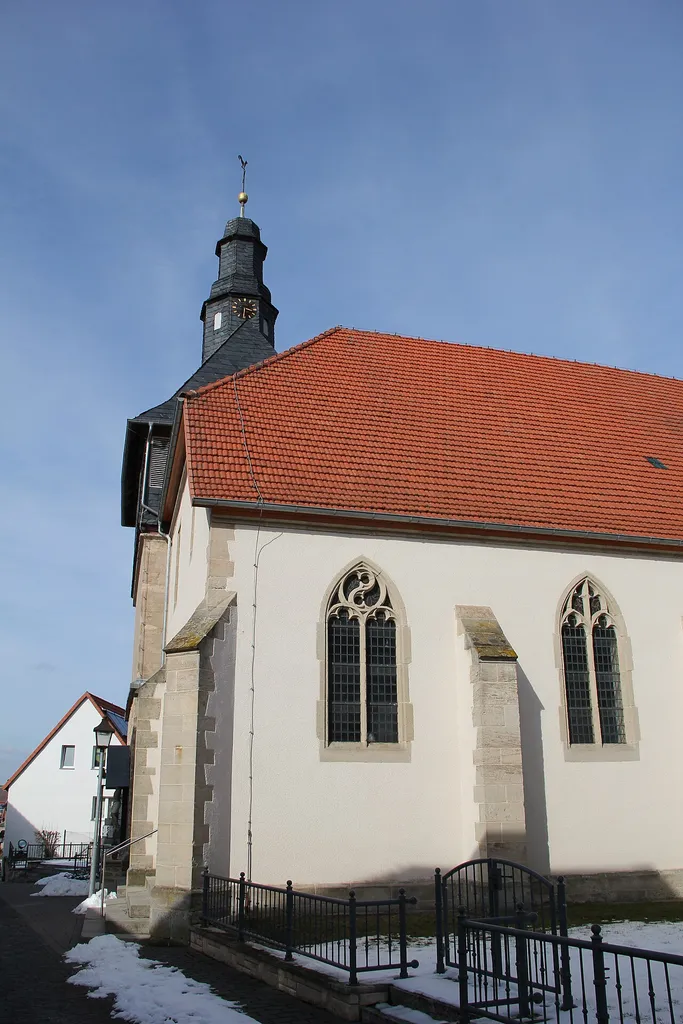 Sankt-Johannes-der-Täufer-Kirche in Jützenbach. Die Kameraposition müsste hier wohl in einem Ast der Jützenbacher Straße sein, welcher dann voraus an der Feuerwehr wieder auf den Hauptast stößt und auf diesem dann an der nord-westlichen Ecke von Nr. 17. Rechts ist die Kirche zu sehen und hinter dieser schaut noch die Giebelwand der Nr. 25 hervor. Die Kameraposition dürfte dann ca. bei 51.524460°, 10.377941° liegen, mit einem Blickwinkel von 22.99