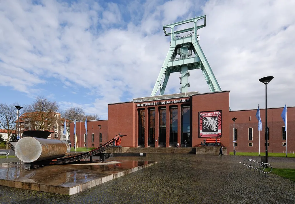 Central segment of the German Mining Museum, Bochum. Architect: Fritz Schupp. In the foreground there is the kinetic sculpture "Base Metals" by Prof. Ovis Wende, 1990. The winding tower was originally built for the Germania mine in Dortmund but was transferred to the museum in 1973. It has a height of 71.4 m and a mass of about 650 tons. There is a sign for the special exhibition on the Courrières mine disaster in 1906.