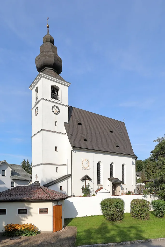 Südwestansicht der röm.-kath. Pfarrkirche Mariä Himmelfahrt in der oberösterreichischen Gemeinde Zell am Moos.Eine spätgotische Kirche mit einem einschiffigen, vierjochigen Langhaus und einem viergeschossigen Westturm mit barockem, birnenförmigem Helm, die 1672 teilweise umgebaut wurde.