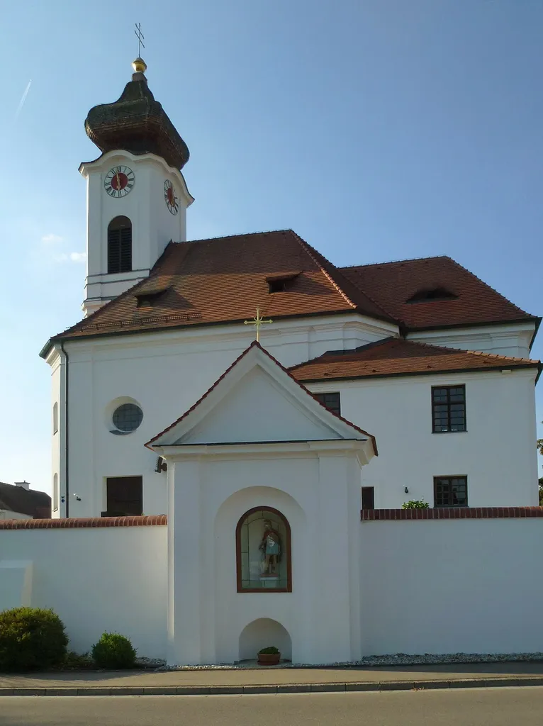 Sigmertshausen, Kirchenstr.15: Katholische Filialkirche St. Maria und Vitalis. Friedhofsmauer mit halbrunden Deckziegeln. Kapellenanbau in die südliche Friedhofsmauer; straßenseitig eine Nische mit einer St. Florians-Statue. Ansicht aus S